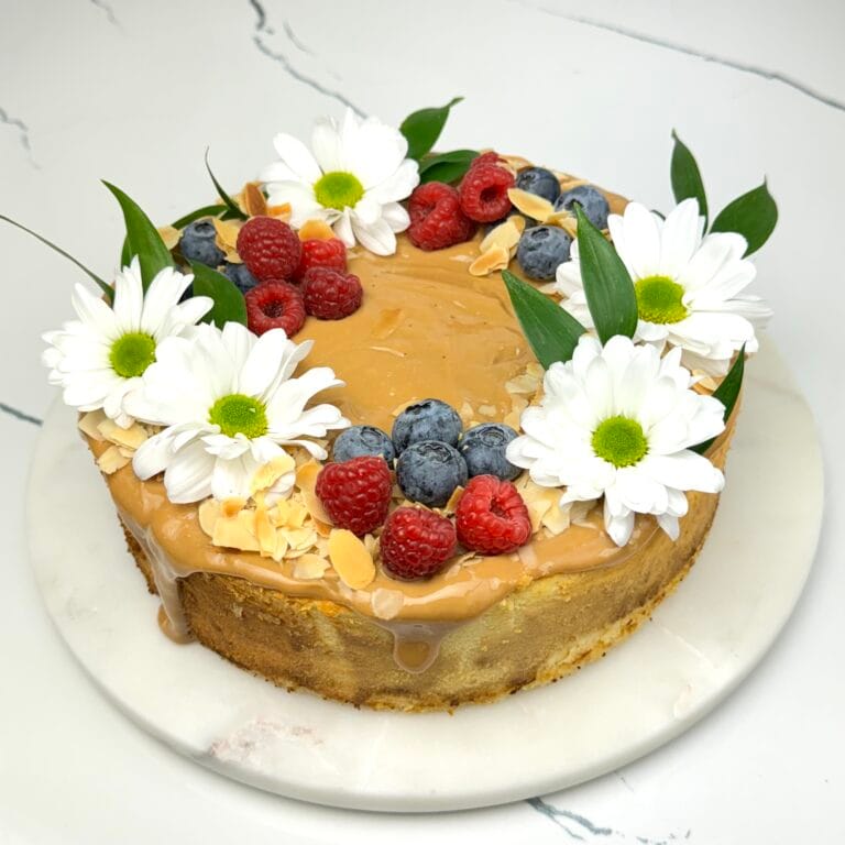 Zdjęcie przedstawia sernik z kajmakiem i płatkami migdałów możliwy do zamówienia przez sklep cukierni Bezownia znajdującej się w Warszawie, ul. F. Joliot-Curie 11