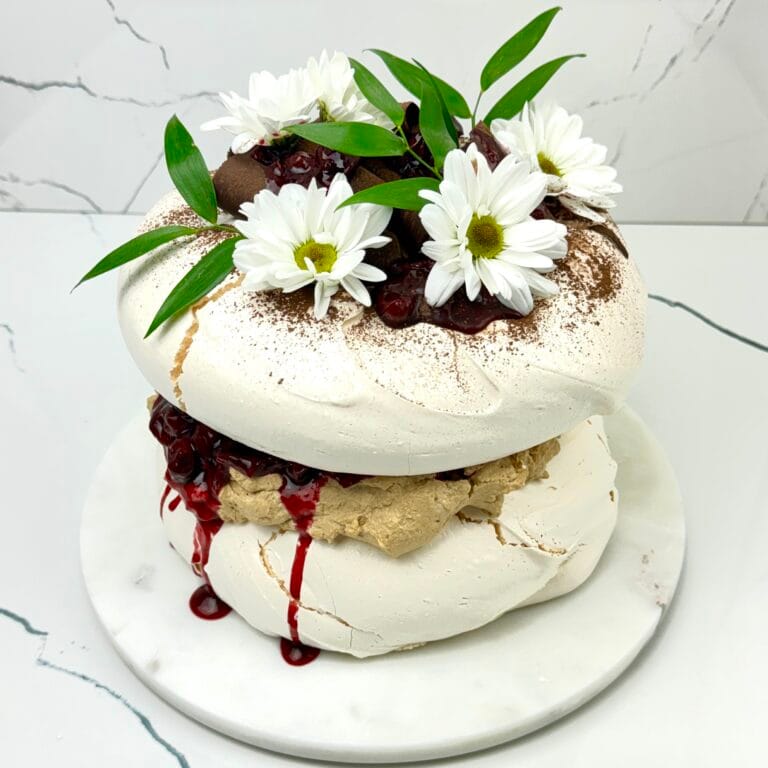 Zdjęcie przedstawia tort bezowy kawowo-wiśniowy możliwy do zamówienia przez sklep cukierni Bezownia znajdującej się w Warszawie, ul. F. Joliot-Curie 11