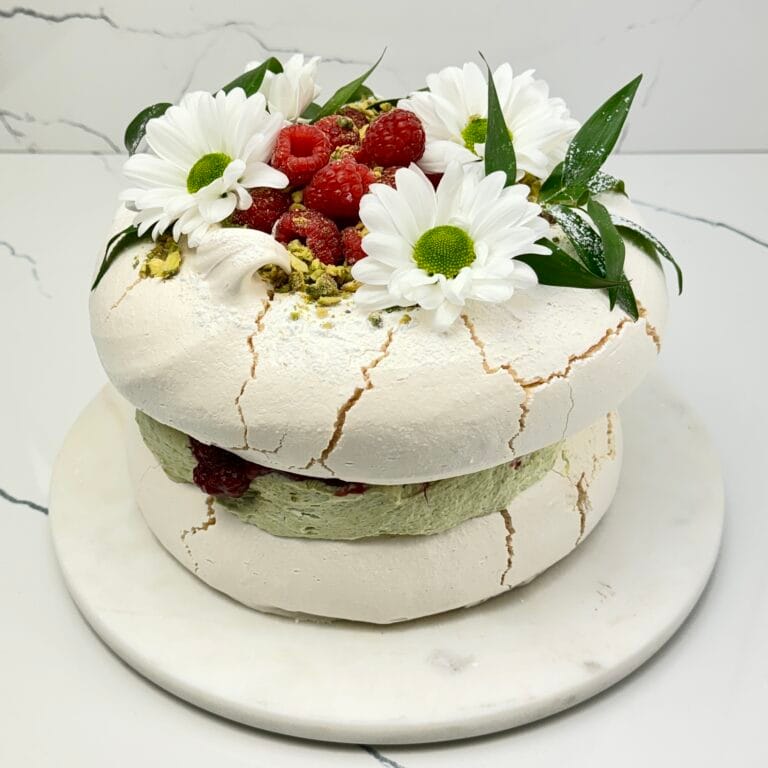 Zdjęcie przedstawia tort bezowy pistacjowo malinowy, który można zamówić przez sklep internetowy cukierni Bezownia znajdującej się w Warszawie, ul. F. Joliot-Curie 11.