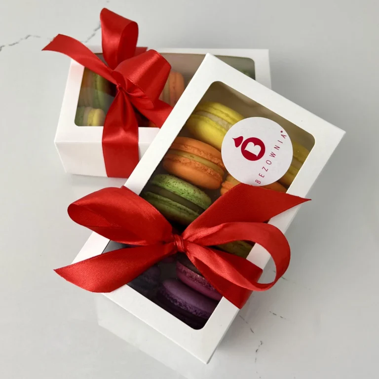 Zdjęcie przedstawia gotowy zestaw do zakupu - makaroniki w białym opakowaniu przewiązane czerwoną kokardką w 5 smakach - zestaw 10 możliwy do zamówienia przez sklep cukierni Bezownia znajdującej się w Warszawie, ul. F. Joliot-Curie 11