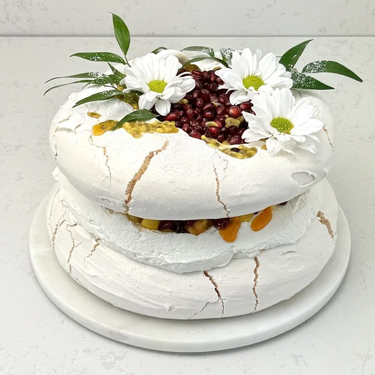 Zdjęcie przedstawia tort bezowy mango granat marakuja możliwy do zamówienia przez sklep cukierni Bezownia znajdującej się w Warszawie, ul. F. Joliot-Curie 11