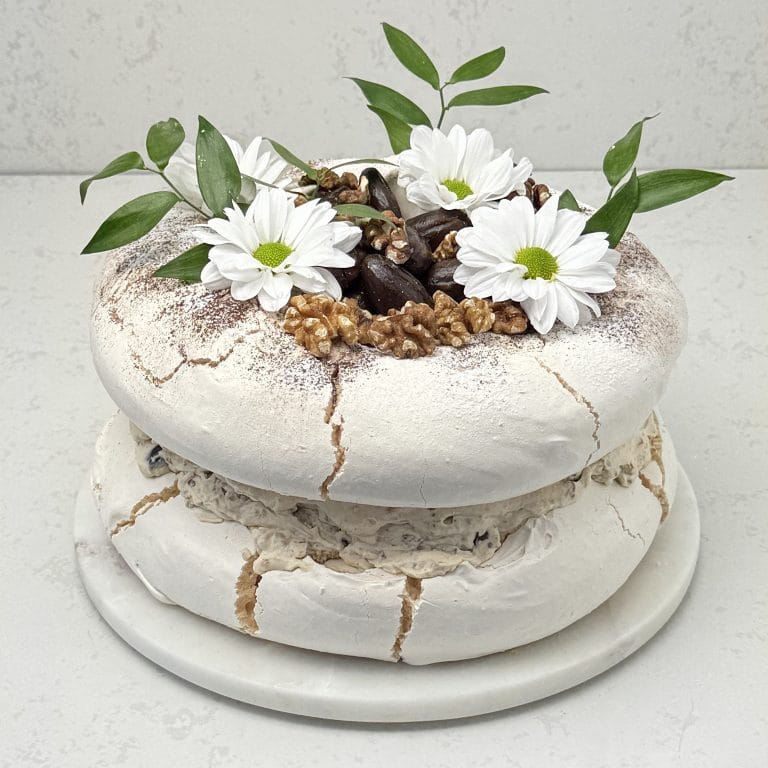 Zdjęcie przedstawia tort bezowy kajmkowy z orzechami włoskimi i daktylami możliwy do zamówienia przez sklep cukierni Bezownia znajdującej się w Warszawie, ul. F. Joliot-Curie 11