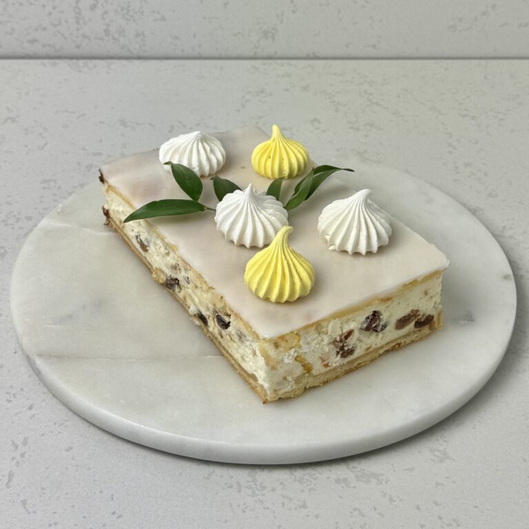 Zdjęcie przedstawia sernik krakowski ozdobiony kolorowymi bezikami. Sernik można zamówić na Wielkanoc przez sklep cukierni Bezownia znajdującej się w Warszawie, ul. F. Joliot-Curie 11.