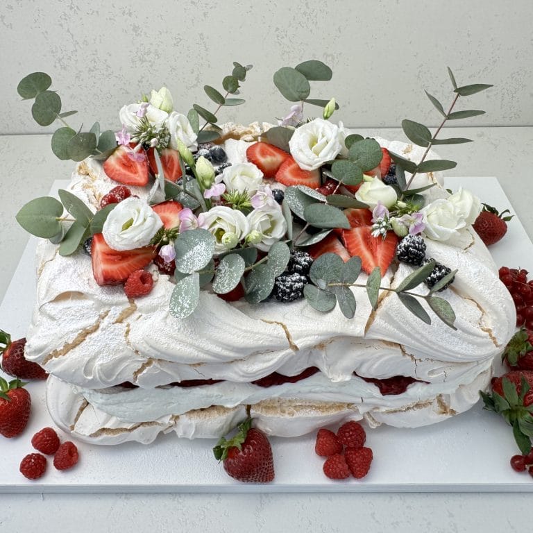 Zdjęcie przedstawia tort bezowy prostokątny z musem malinowym i świeżymi owocami, który można zamówić przez sklep cukierni Bezownia znajdującej się w Warszawie, ul. F. Joliot-Curie 11.