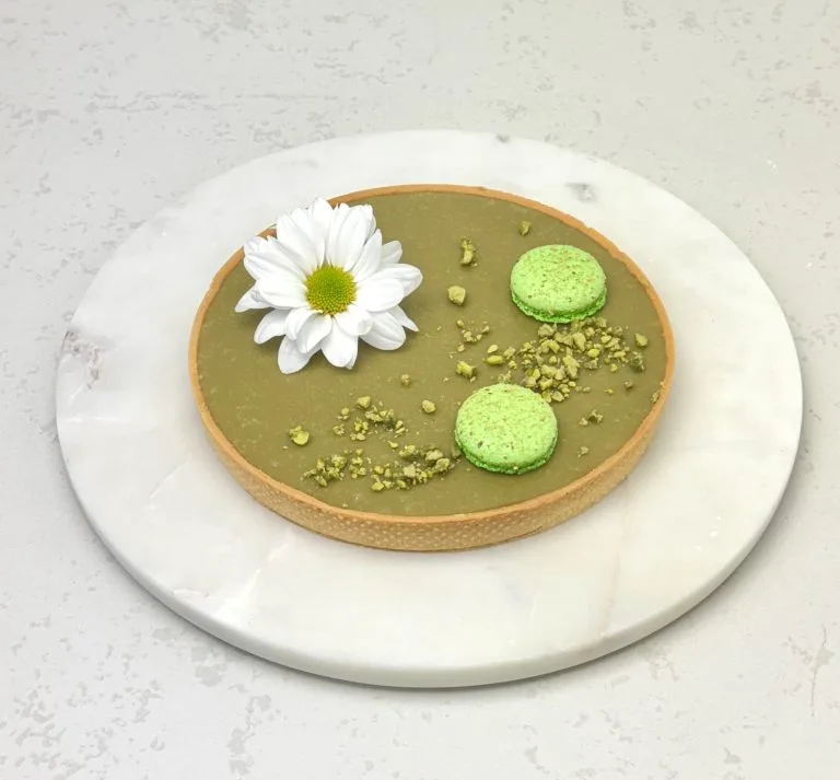 Zdjęcie przedstawia tartę pistacjową, którą można zamówić przez sklep cukierni Bezownia znajdującej się w Warszawie, ul. F. Joliot-Curie 11.