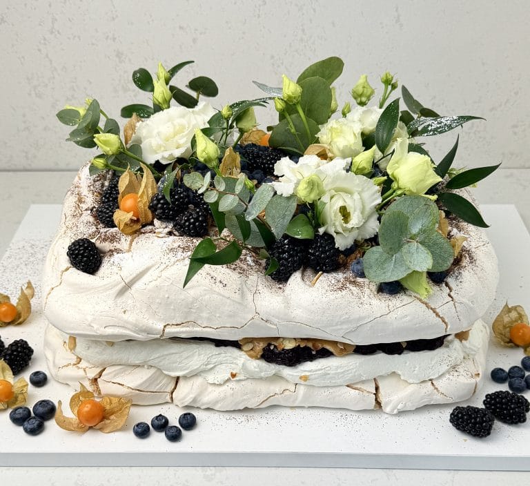 Zdjęcie przedstawia tort bezowy prostokątny z musem z czarnej porzeczki, kajmakiem i migdałami, który można zamówić przez sklep cukierni Bezownia znajdującej się w Warszawie, ul. F. Joliot-Curie 11.