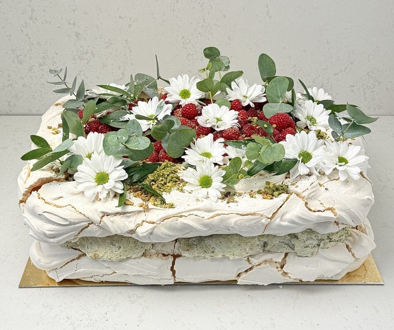 Zdjęcie przedstawia tort bezowy prostokątny z kremem pistacjowym i musem malinowym, który można zamówić przez sklep cukierni Bezownia znajdującej się w Warszawie, ul. F. Joliot-Curie 11.