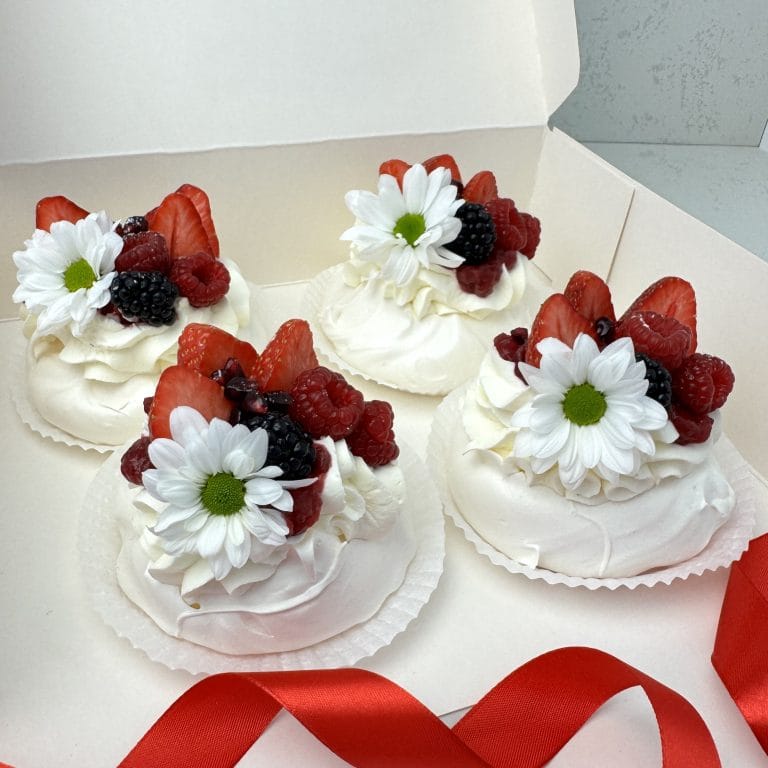 Zdjęcie przedstawia 4 beziki mini Pavlova udekorowane świeżymi owocami i kwiatami - możliwe do zamówienia przez sklep cukierni Bezownia znajdującej się w Warszawie przy ul. Joliot-Curie 11.