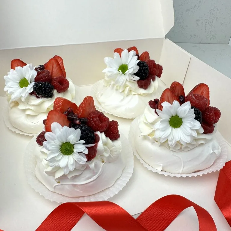 Zdjęcie przedstawia 4 beziki mini Pavlova udekorowane świeżymi owocami i kwiatami - możliwe do zamówienia przez sklep cukierni Bezownia znajdującej się w Warszawie przy ul. Joliot-Curie 11.