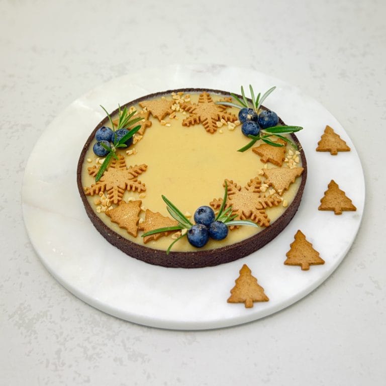 Zdjęcie przedstawia świąteczną tartę fistaszkową udekorowaną pierniczkami. Tarta możliwa jest do zamówienia przez sklep cukierni Bezownia znajdującej się w Warszawie, ul. F. Joliot-Curie 11.