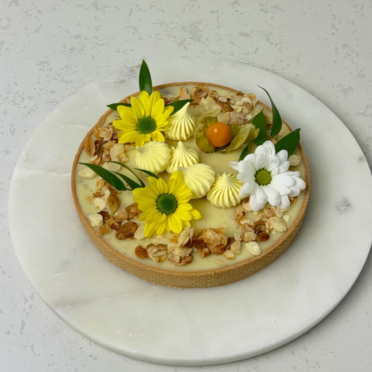 Zdjęcie przedstawia tartę z białą czekoladą i czarną porzeczką w świątecznej odsłonie. Tartę można zamówić przez sklep cukierni Bezownia znajdującej się w Warszawie, ul. F. Joliot-Curie 11.