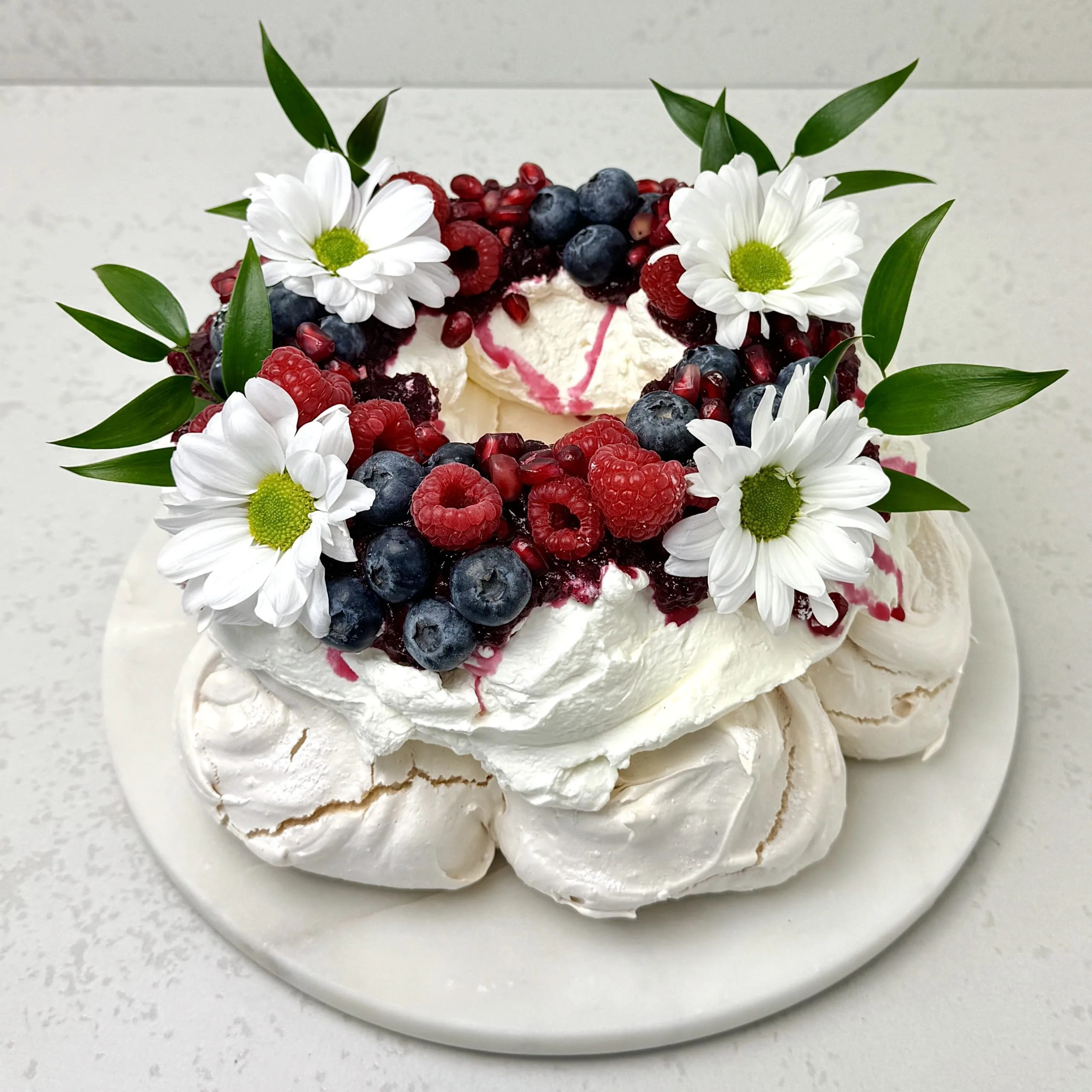 Zdjęcie przedstawia tort bezowy Pavlova z żurawiną i świeżymi owocami sezonowymi, który można zamówić przez sklep cukierni Bezownia znajdującej się w Warszawie, ul. F. Joliot-Curie 11.