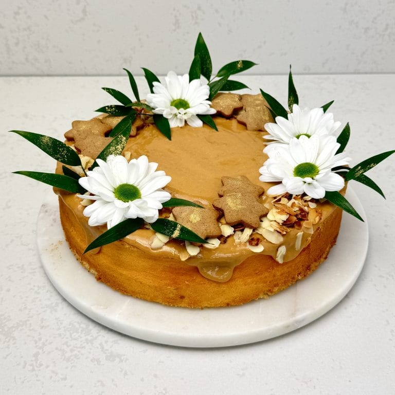 Zdjęcie przedstawia sernik przykryty kajmakiem i udekorowany świeżymi kwiatami. Sernik można zamówić przez sklep cukierni Bezownia znajdującej się w Warszawie, ul. F. Joliot-Curie 11.