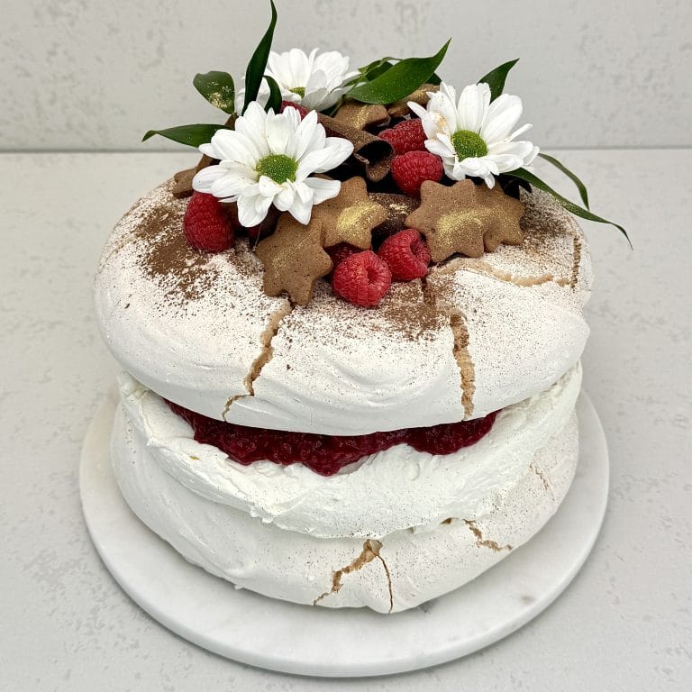 Zdjęcie przedstawia tort bezowy z musem malinowym w świątecznej odsłonie, który można zamówić przez sklep cukierni Bezownia znajdującej się w Warszawie, ul. F. Joliot-Curie 11.