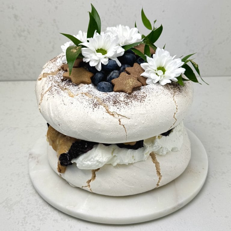 Zdjęcie przedstawia tort bezowy z czarną porzeczką w świątecznej odsłonie. Tort można zamówić przez sklep cukierni Bezownia znajdującej się w Warszawie, ul. F. Joliot-Curie 11.