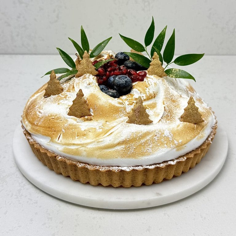 Zdjęcie przedstawia świąteczną tartę cytrynową udekorowaną pierniczkami. Tarta możliwa jest do zamówienia przez sklep cukierni Bezownia znajdującej się w Warszawie, ul. F. Joliot-Curie 11.