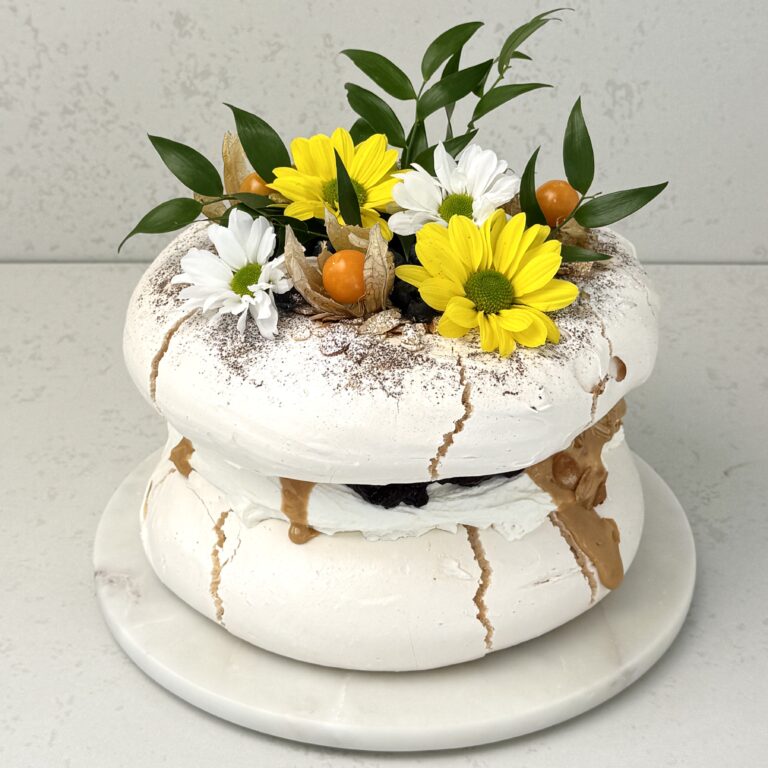 Zdjęcie przedstawia tort bezowy z czarną porzeczką w świątecznej odsłonie. Tort można zamówić przez sklep cukierni Bezownia znajdującej się w Warszawie, ul. F. Joliot-Curie 11.