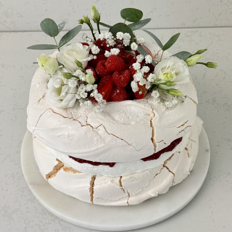 Zdjęcie przedstawia tort bezowy z musem malinowym, który można zamówić przez sklep cukierni Bezownia znajdującej się w Warszawie, ul. F. Joliot-Curie 11.